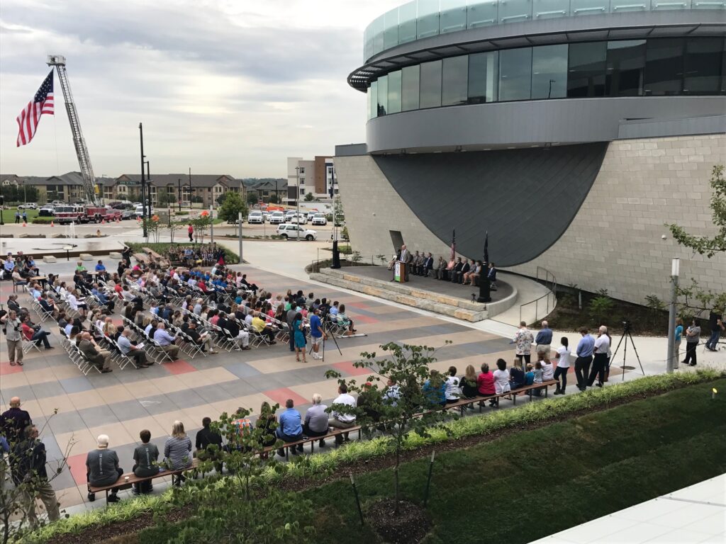 Lenexa Civic Center Ribbon Cutting Ceremony with large audience and American flag.