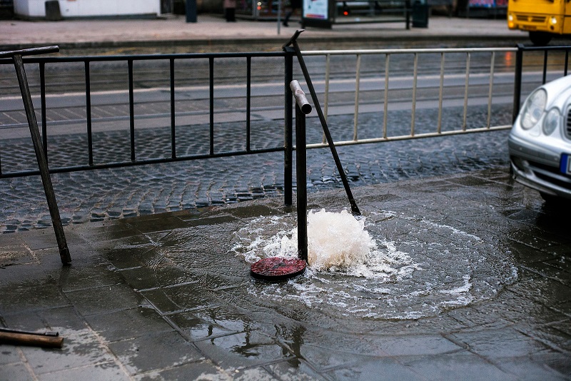 Broken sewer drain on city street needing stormwater repair. Flooding water flows out of manhole.