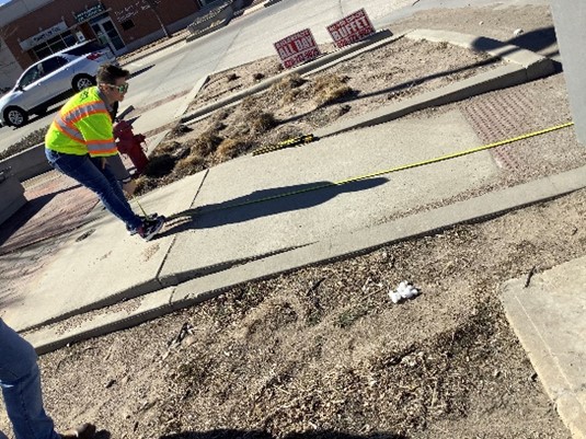Man with tape measure measuring the length of a sidewalk to be ADA design compliant for the state of kansas.